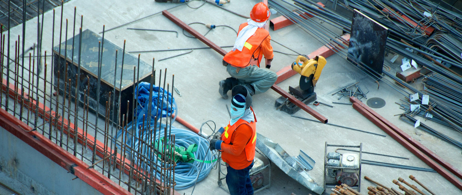 Two engineers wearing bright orange high-vis jackets at work on a large building site